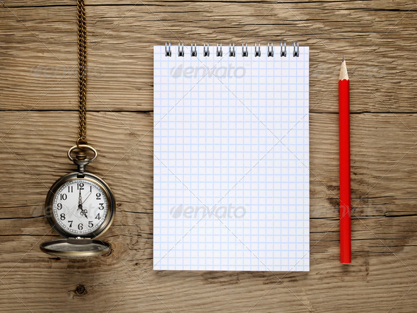 Pocket watch, pencil and note book on old wooden background