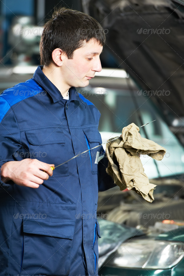 auto mechanic technician examining level during replacing and pouring motor oil into automobile engine at maintenance repair service station