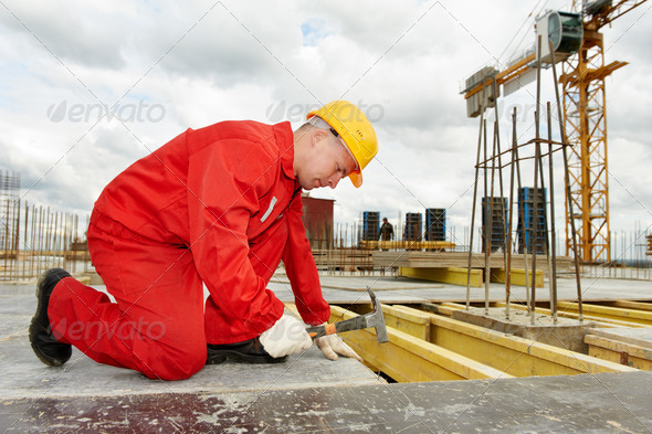 builder in uniform working with hammer and nail at construction site
