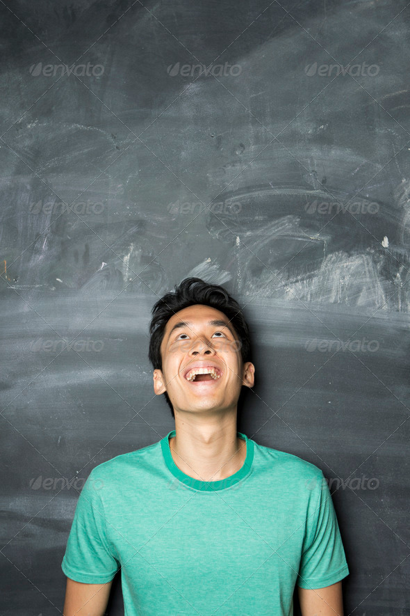 Happy Asian man looking above at empty blackboard.