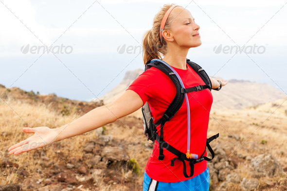 Young woman runner enjoying summer day in mountains with arms outstretched. Female jogger exercising outdoors in nature, La Gomera Canary Islands.