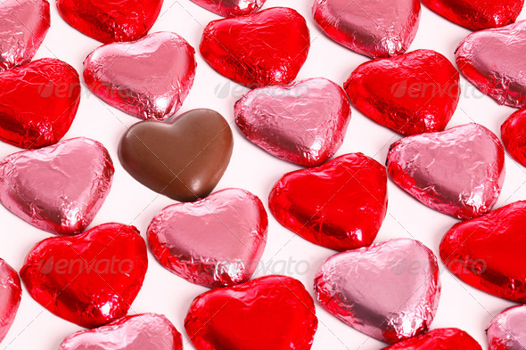 Chocolate hearts in red and pick foil wrappers on a white background, with one unwrapped heart in amongst the group.