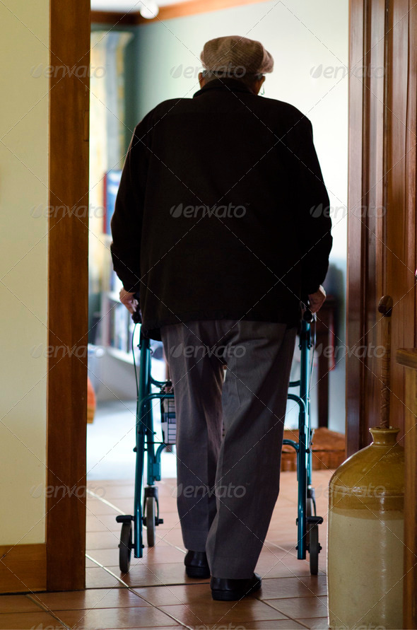 An old disabled elderly man who need additional support to maintain balance or stability while walking use a walker (walking frame) in his house.