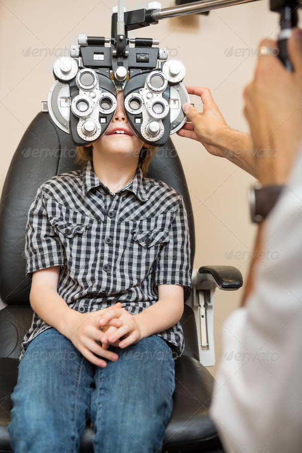 Preadolescent boy undergoing eye examination with phoropter in store