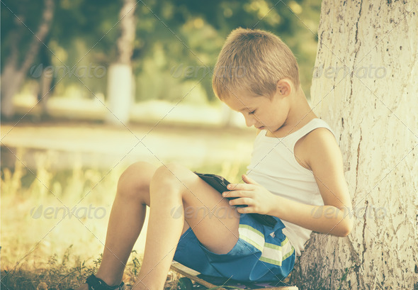 Boy Child playing with Tablet PC Outdoor with Summer nature
