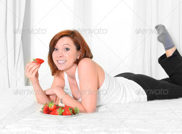 Young Attractive woman eating a bowl of strawberries in bed