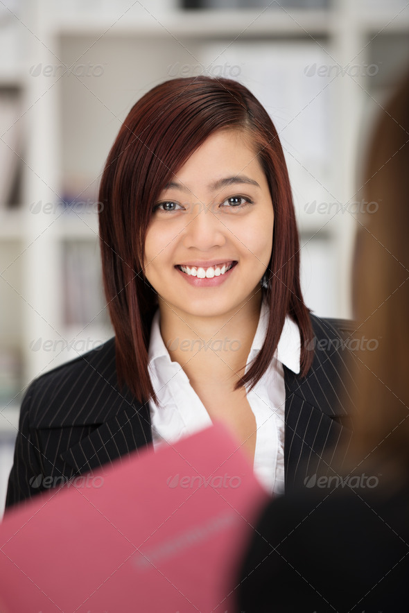 Happy successful young female Asian job applicant in a stylish jacket looking at the camera with a smile as she clutches her curriculum vita