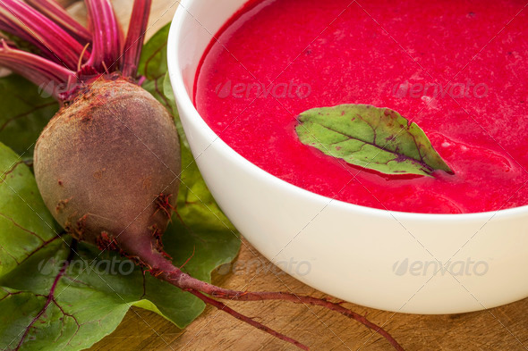 a bowl of cream soup of red beets with a fresh beet root and leaves