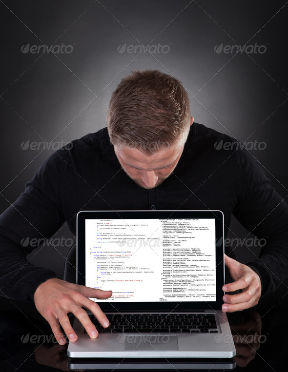 Man or hacker stealing data from a laptop at night bending forwards over the keyboard in the glow from the screen as he browses the internet or retrieves and downloads personal data